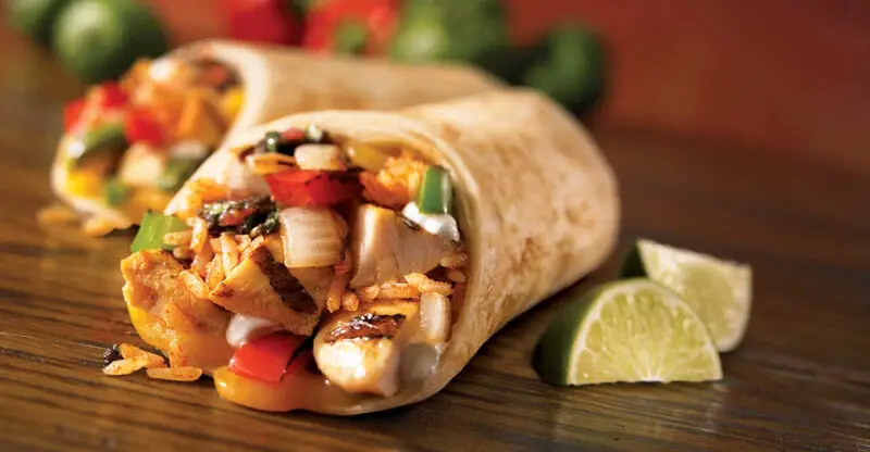 Close-up of a chicken and rice burrito with lime wedges