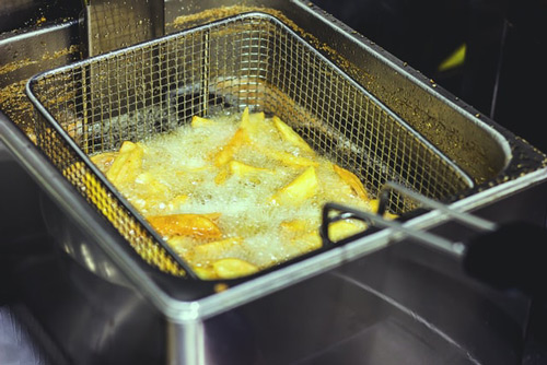 Close-up of french fries deep frying in a metal fryer