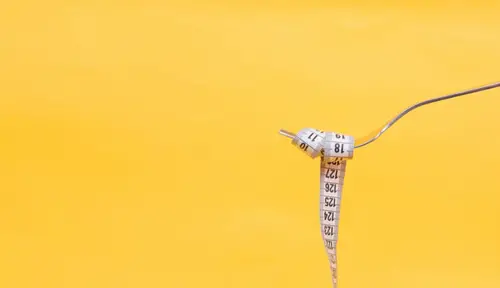 A tape measure wrapped around a fork against a bright yellow background
