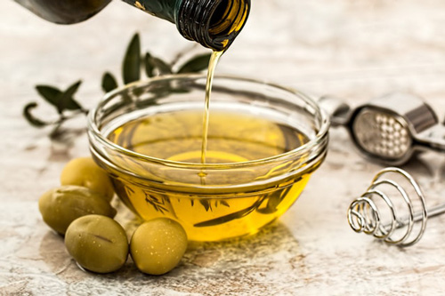 Up close image of olive oil dripping into a glass bowl placed on a countertop