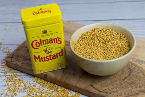 A can of Coleman dry mustard powder and bowl of yellow mustard seeds